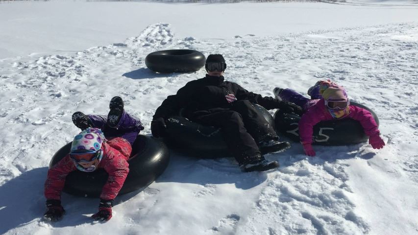 family of three on winter tubing hill in snow